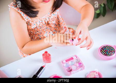 Asian adorabile divertente ragazza che fa makeup tuffi pennello in bottiglia per dipingere unghie lucidare vernice rossa chiodo lei stessa, attività di apprendimento per essere donna, Foto Stock