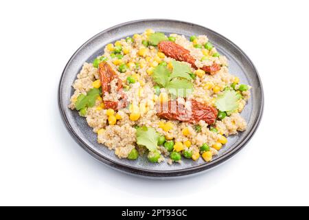 Porridge di quinoa con piselli verdi, mais e pomodori secchi su piastra di ceramica isolata su fondo bianco. Vista laterale, primo piano. Foto Stock