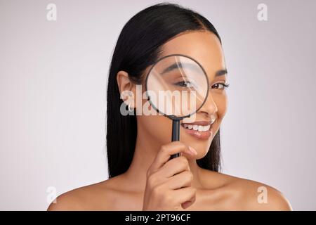 Diamo un'occhiata più da vicino. Studio ritratto di una giovane donna attraente guardando attraverso una lente di ingrandimento su uno sfondo rosa Foto Stock