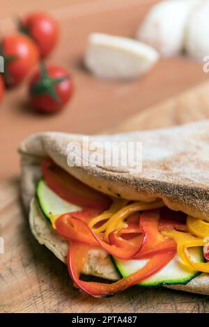 Cucina italiana, pizza calzone chiusa su sfondo rustico in legno. Sullo sfondo piccoli pomodori rossi, mozzarella e basilico. Messa a fuoco selettiva. Foto Stock