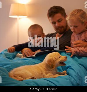 È stata una giornata divertente, ma ora è stanco...Un padre che legge una storia di andare a letto ai suoi figli Foto Stock