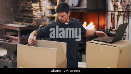 Assicurarsi che tutto sia in ordine per essere spedito per la consegna. un uomo che utilizza un computer portatile mentre ordina gli ordini e le consegne nella sua officina Foto Stock