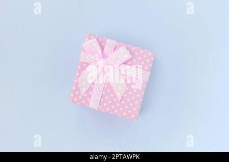 Piccola rosa confezione regalo con nastro giace su un sfondo violetto. Il minimalismo laici piatta vista dall'alto. Foto Stock