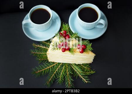 Pezzo di torta decorata ad albero e frutti di bosco su un fondo nero con due tazze di caffè. Foto Stock