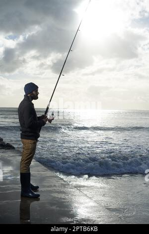 Prendendosi il suo tempo per la grande cattura. Foto a tutta lunghezza di un pescatore solista che pesca da un molo all'oceano Foto Stock