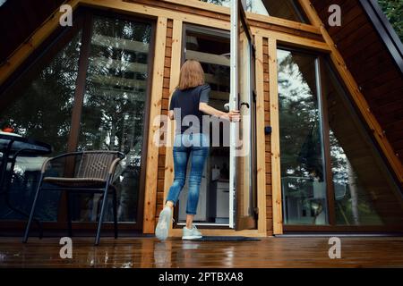 Vista posteriore di una donna che entra nella cabina forestale Foto Stock