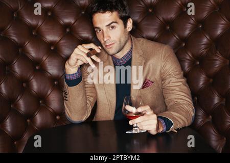 Amo un buon sigaro con il mio whiskey. Ritratto di un bel giovane che beve e fuma un sigaro in un club Foto Stock