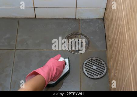 Donna che pulisce il pavimento del bagno che è molto sporco. Foto Stock