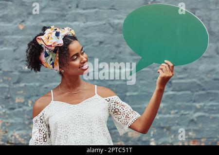 Amate le parole che parlate essendo sempre gentili. una giovane donna attraente che tiene una bolla di discorso contro un muro di mattoni all'esterno Foto Stock