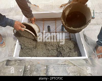 Versando il mortaio versando il calcestruzzo pronto-mescolato sulla maglia di filo Foto Stock