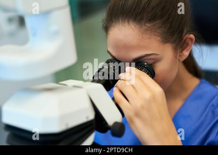 A volte gli occhi hanno bisogno di un piccolo aiuto. un giovane patologo che guarda i campioni al microscopio Foto Stock