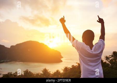 La vacanza dei sogni. Ripresa da dietro di un giovane turista che alza le braccia contro una vista al tramonto Foto Stock