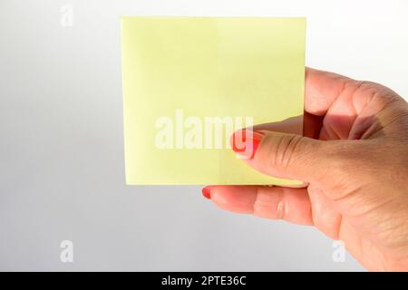 Mano della donna con le unghie verniciate che tengono la carta bianca della lettera su fondo bianco puro. Foto Stock