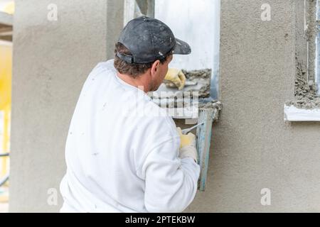 Stuccatore intonaco di livellamento su una facciata permanente sulla impalcatura Foto Stock