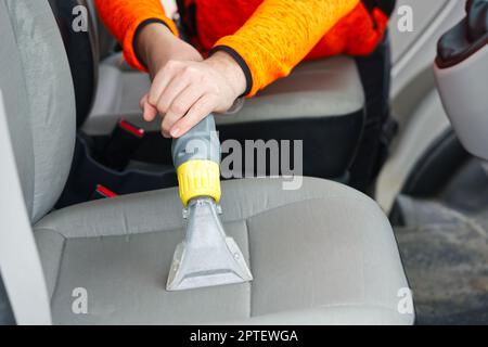 Sedile anteriore in tessuto per auto con aspirapolvere per uomo. uomo che pulisce la macchina da lavoro Foto Stock