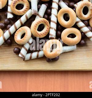 Tubuli croccanti, palline di cioccolato fondenti e bagel giacciono su una superficie di legno. Mix di dolci vari Foto Stock