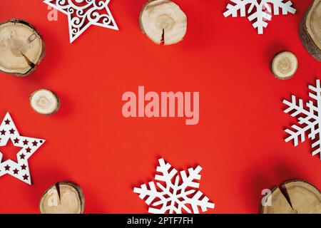 Tagli di legno o bramme di ramo e fiocchi di neve di legno su sfondo rosso. Natale o Capodanno. Disposizione piatta. Spazio di copia Foto Stock