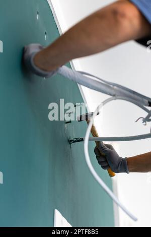 Primo piano del chiodo martellante nella parete. L'operatore maschio guida i perni nella parete prima di installare il condizionatore d'aria. Vista dal basso ad angolo delle mani che tengono hamme Foto Stock