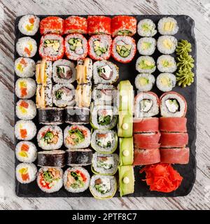 Ampia varietà assortita di sushi rolls serviti su ardesia di metallo nero su tavolo di legno. Vista dall'alto del set di sushi composto da sushi roll con riempimento diverso Foto Stock