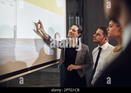 Parlare numeri con il suo team. un dirigente che offre una presentazione su uno schermo di proiezione a un gruppo di colleghi in una sala riunioni Foto Stock