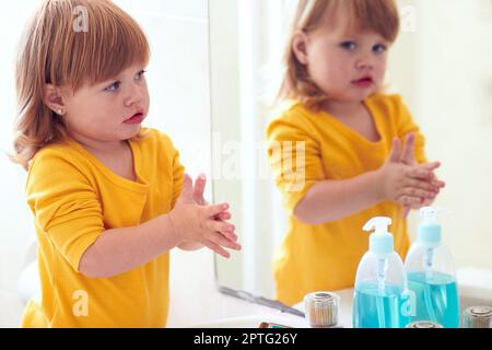 Facendolo il modo in cui la mamma mi ha insegnato. una bambina che guarda nello specchio mentre si lava le mani Foto Stock