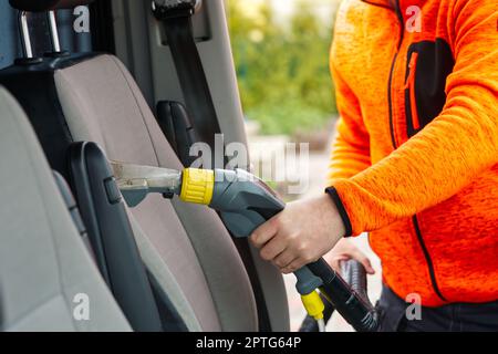 Sedile anteriore in tessuto per auto con aspirapolvere per uomo. uomo che pulisce la macchina da lavoro Foto Stock