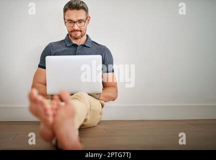 Controllare i feed dei social media. un uomo che usa il computer portatile mentre si siede a una parete Foto Stock