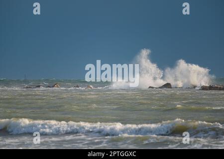 Le onde grandi si arrotolano sulla spiaggia. Vicino al parasol in giorno di sole luminoso. Bianco schiumoso onde e spruzzi. Una calda giornata estiva e alta onda, stagcape.Italy Foto Stock