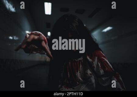 Trucco halloween sanguinante. Donna asiatica zombie con sangue che muore e spaventata a notte buia in tunnel, Horror sanguinoso fantasma ragazza capelli coprire viso Foto Stock