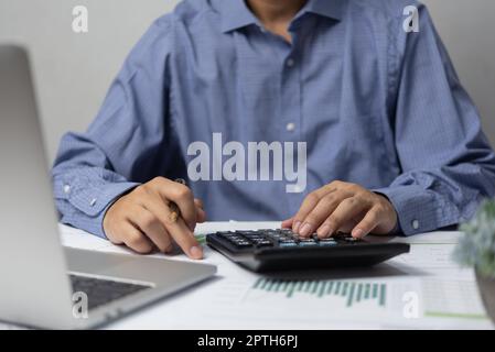 Mano di uomo d'affari usando la penna di ritegno della calcolatrice e con fare la contabilità di imposta e di finanza sulla scrivania all'ufficio domestico. Foto Stock