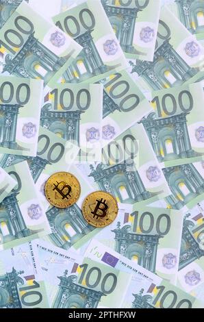 Le bitcoins fisiche dorate si trovano su un insieme di tagli monetari verdi di 100 euro. Un sacco di soldi forma un mucchio infinito Foto Stock