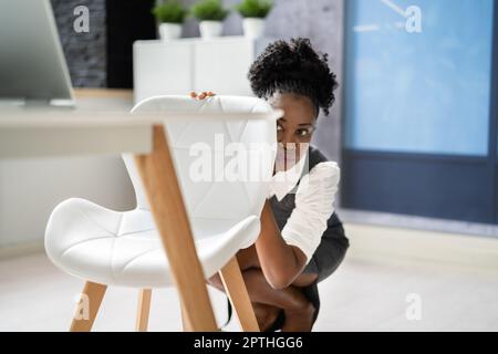 Spaared Female Hiding sotto scrivania in ufficio Foto Stock