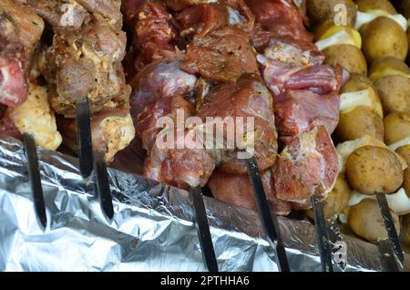 La carne cruda e le patate sono piantati su spiedini di metallo. Il processo di cottura shish kebab. Russo e ucraino cibo camp Foto Stock