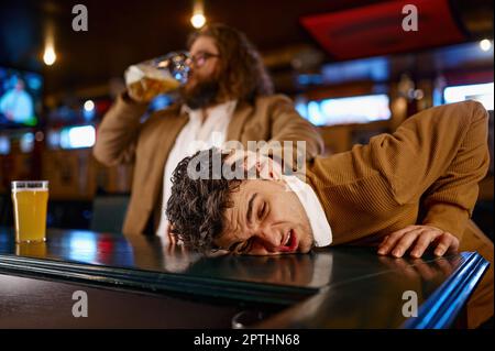 Comportamento pazzo dei tifosi di calcio al pub sportivo. Uomo che tira la faccia di un altro ragazzo sul banco del bar e beve birra Foto Stock