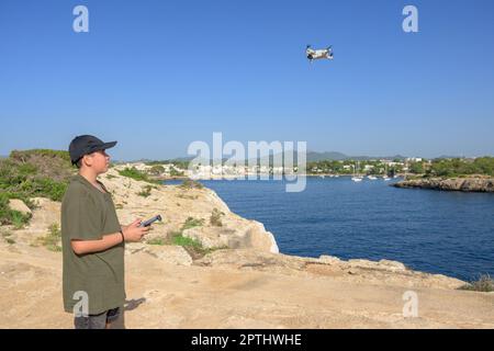 Ragazzo felice, drone volante sulla costa mediterranea, contro il cielo blu durante il giorno di sole Spagna, Isole Baleari, Foto Stock