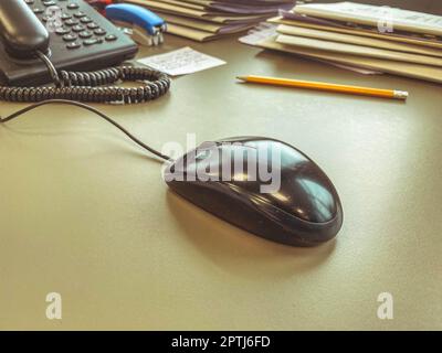 un mouse nero del calcolatore si trova su un tavolo di legno dell'ufficio. attrezzature informatiche per il lavoro. mouse per clic, lavorare dietro il monitor. comodità dei dipendenti. Foto Stock