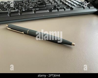 Penna a sfera verde automatica per scrivere sulla scrivania dell'ufficio con tastiera del computer. Lavoro aziendale. Foto Stock