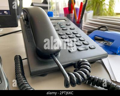 Telefono fisso nero con tubo, pulsanti e filo sul tavolo da lavoro alla scrivania con forniture per ufficio. Lavoro aziendale. Foto Stock