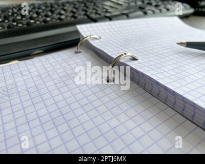 Un blocco note di carta con raccoglitore a spirale e fogli bianchi vicino alla penna di plastica nera giace di tavolo da ufficio blu. Vista dall'alto. Copia spazio per. Foto Stock