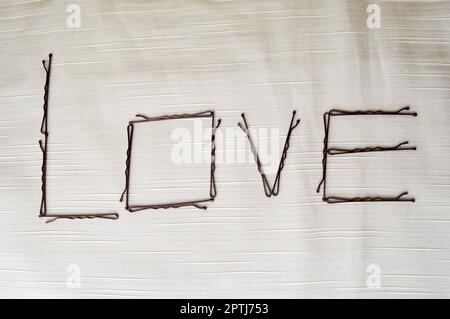Scrivi un amore scritto da hairpin-ignorami su uno sfondo beige. La parola amore è composta da ornamenti femminili. Foto Stock