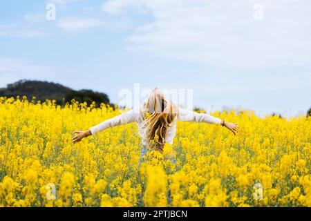 Bella ragazza dai capelli biondi posa in mezzo a un campo di fiori di colza gialli fiorenti Foto Stock