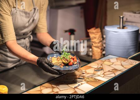 Primo piano dello chef che dà fuori il piatto finito alla stazione di ordinazione in cucina ristorante aperto Foto Stock