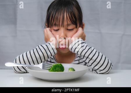 Ai bambini non piace mangiare verdure. Ragazza asiatica cute che rifiuta di mangiare verdure sane. Alimentazione e abitudini alimentari sane per i bambini. Foto Stock