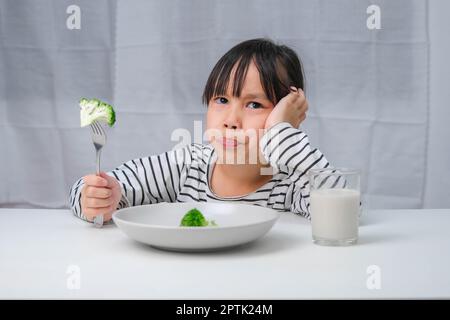 Ai bambini non piace mangiare verdure. Ragazza asiatica cute che rifiuta di mangiare verdure sane. Alimentazione e abitudini alimentari sane per i bambini. Foto Stock