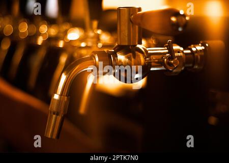 Immagine creativamente sfocata dei rubinetti in birreria con bokeh sfocato e rumore digitale artistico. Fila dorata di rubinetti nella stanza del rubinetto. Immagine di sfondo della barra Foto Stock