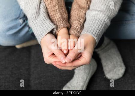 Donne che tengono la mano dei figli, il maglione lavorato a maglia e i calzini sullo sfondo. Riscaldamento casa e concetto di famiglia. Foto Stock