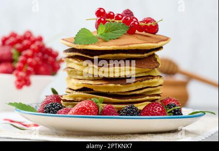 Accatastate le frittelle cotte con la frutta in un piatto rotondo su un tavolo bianco Foto Stock