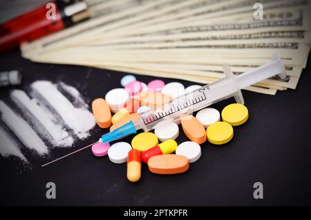 linee di cocaina, siringa, compresse e dollari su un tavolo nero Foto Stock