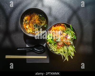 Pranzo in stile asiatico. Zuppa di miso Shiro e ciotola di poke con salmone, cetrioli, fagioli verdi, carote e insalata di chukka Foto Stock