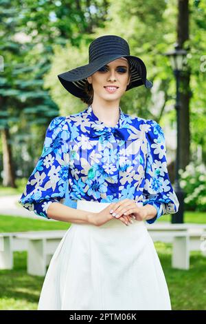 Ritratto all'aperto di una ragazza sorridente in berretto nero, blusa blu e gonna bianca. Foto Stock